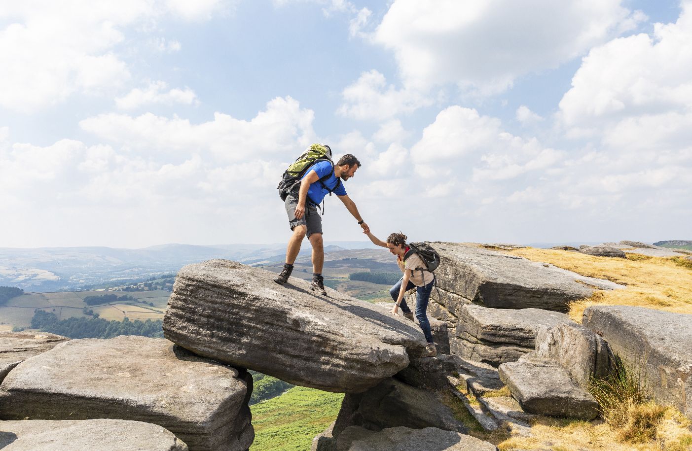 UK, Peak District, people helping each other to climb on top of a rock